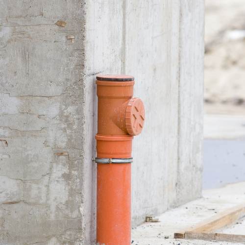 A large red sewer pipe extends out of concrete near a wall.