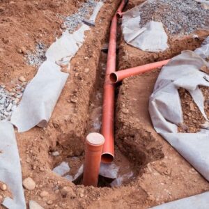 New sewer line pipes are sitting over an exposed earth trench during the installation process.