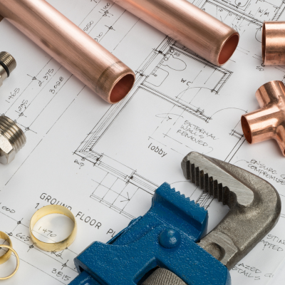 Copper pipes and fittings, a blue pipe wrench, and plumbing rings on a detailed architectural drawing of building plumbing plans,
